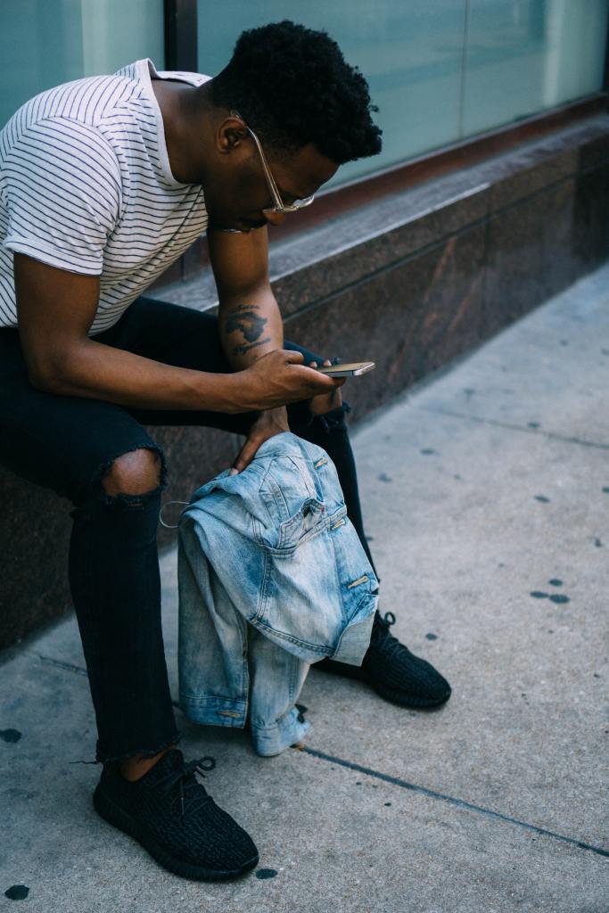 A Black person in a black and white striped shirt sitting and looking down at their phone